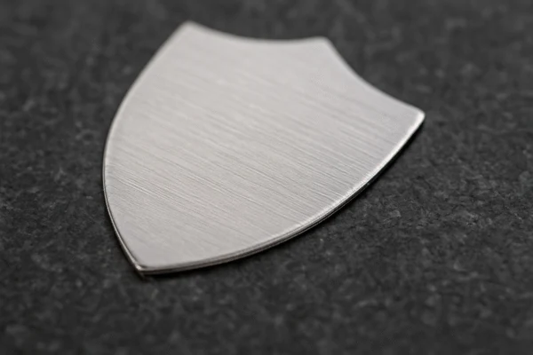 Brushed stainless steel stamped shield plate, custom sheet metal component photographed on a dark textured surface.