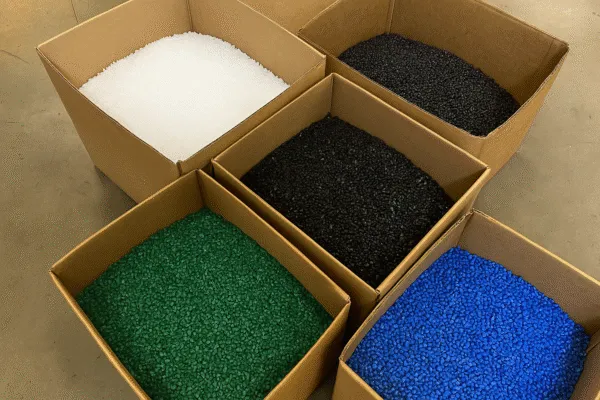 Colorful plastic pellets in white, black, green, and blue, stored in cardboard boxes ready for manufacturing.