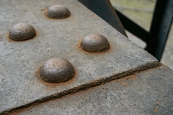Close-up view of metal rivets or bolts on a steel surface, showing rust and weathering.