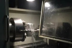 CNC lathe turning operation inside the machine enclosure, with metal chips forming during precision machining.