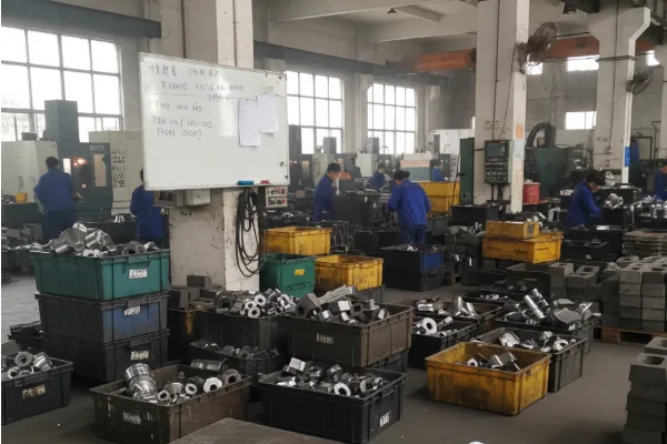 CNC machining workshop with multiple bins of machined metal components and operators working on the production floor.