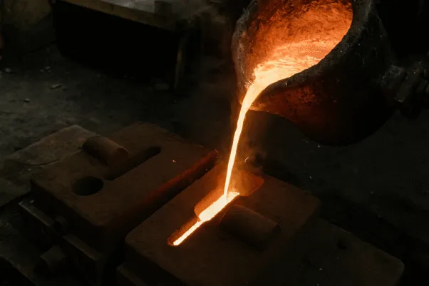 Molten metal being poured into a casting mold, glowing brightly in a foundry.