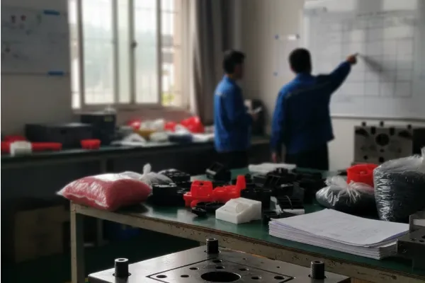 Manufacturing team reviewing a production plan on a whiteboard in a workshop, with molded parts and paperwork on a workbench.