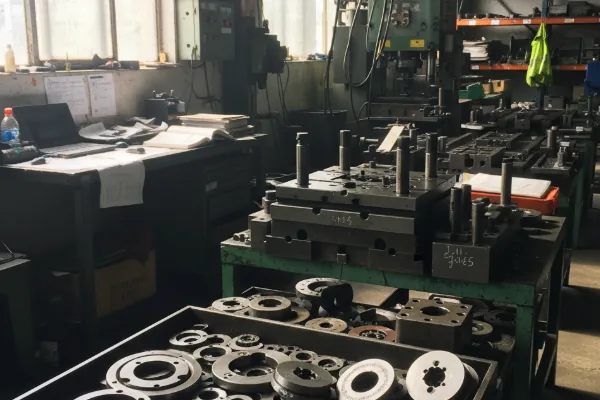 Metal stamping tooling and dies in a workshop, with die sets and machined components arranged on worktables.