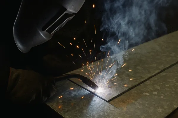 Welder working on galvanized metal, creating sparks and smoke while welding a metal sheet.