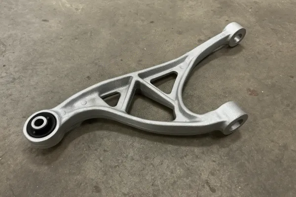 Close-up of a lightweight aluminum suspension arm with a black rubber bushing, used in automotive applications.