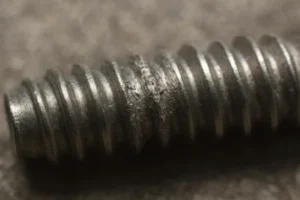 Close-up of a damaged thread on a metal screw, showing wear and tear.