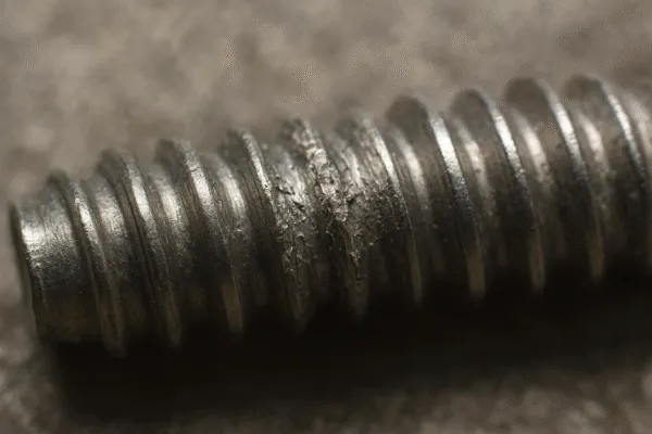 Close-up of a damaged thread on a metal screw, showing wear and tear.