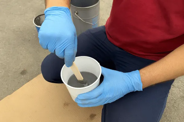 Worker mixing epoxy resin with a stick in a container, preparing for use in manufacturing.