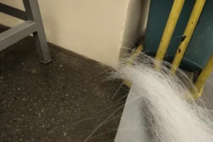 Loose white fiber strands on a workshop floor near equipment, highlighting material handling and cleanliness for quality control.