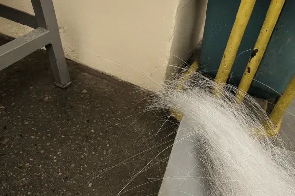 Loose white fiber strands on a workshop floor near equipment, highlighting material handling and cleanliness for quality control.