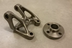 Close-up of two machined metal parts, one with a complex design and the other with a simple round flange.