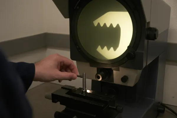 Optical comparator inspecting a threaded fastener on a measurement stage, showing precision dimensional quality control for OEM manufacturing.