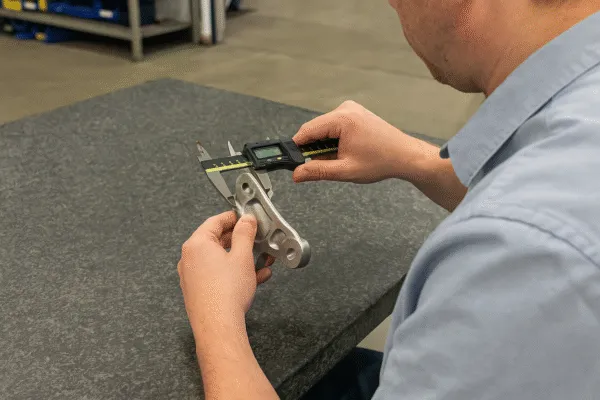 Quality control technician measuring a custom-machined metal part with a digital caliper.