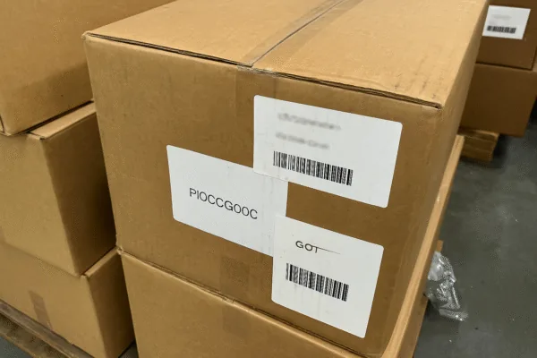 Shipping cartons with barcode labels and part number stickers stacked on a pallet, showing OEM packaging and warehouse logistics.