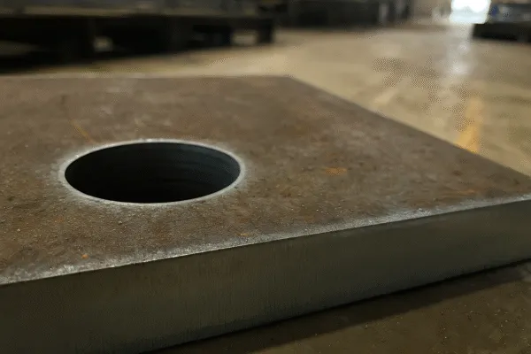 Close-up of a steel plate with a hole, showing the machining quality.
