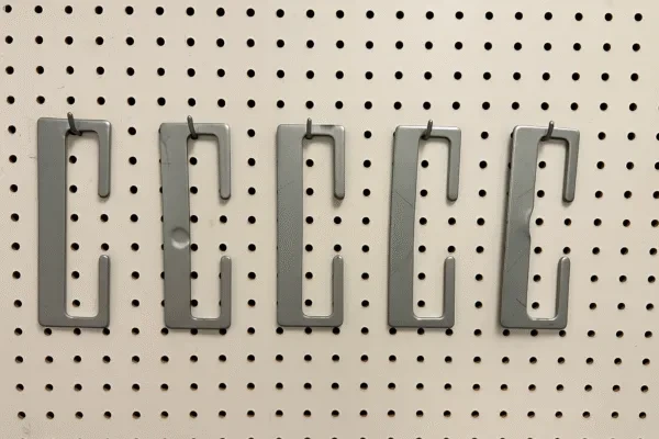 Custom metal stamping hook brackets displayed on a pegboard, showing precision stamped steel parts with clean edges and uniform finish.