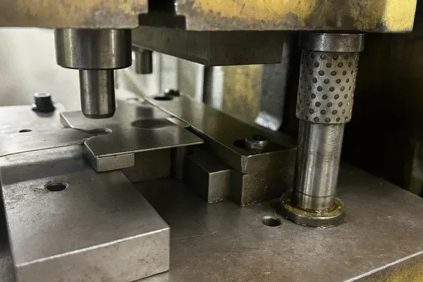 Close-up of a metal stamping die in a press, showing sheet metal positioned for precision punching and forming.