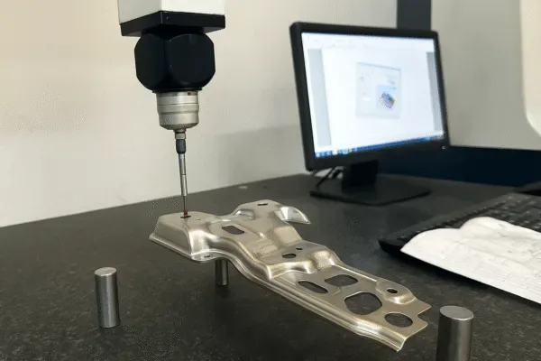 CMM probe measuring a stamped metal component on a granite inspection table with monitor and drawing