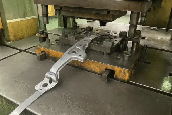 Stamped metal part on a stamping press die, showing progressive tooling setup for sheet metal fabrication