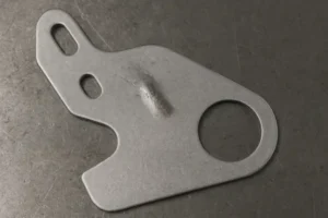 Stamped steel bracket with embossed feature, round hole, and slotted mounting holes on a metal workbench.