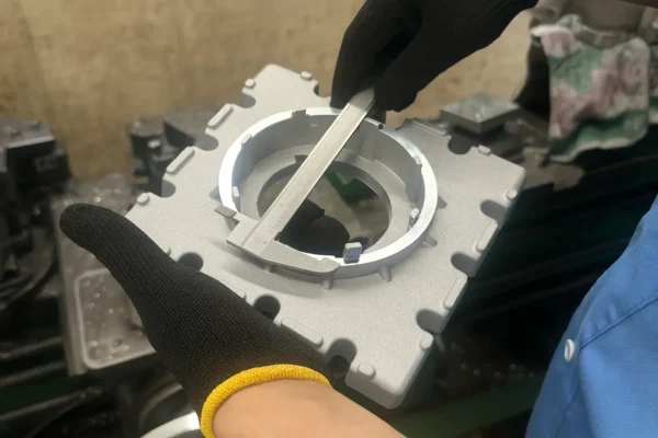 High-resolution image of a caliper measuring the inner diameter of a custom machined alloy component, with the part held by hands wearing black safety gloves.
