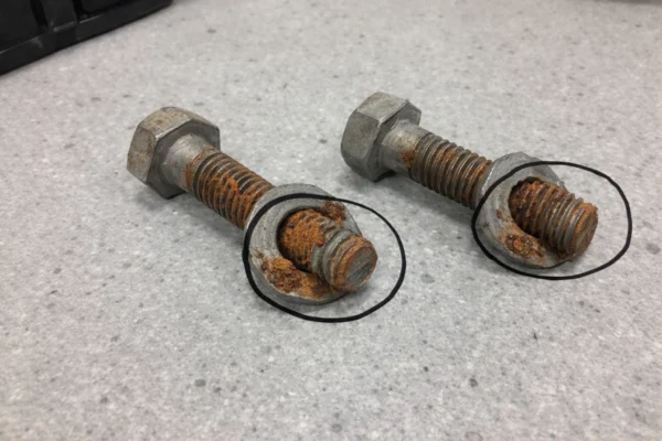 Rusted bolt and washer assemblies on a QC bench, with corrosion at the washer line circled for failure analysis.